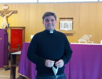 Padre Gabriel Díaz Arzola de pie, con la mascarilla de la mano y sonriendo; en la iglesia de San Vicente de Paúl de Valdemoro