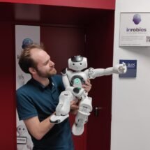 En la imagen aparece José Carlos, director técnico de Irobics, sujetando en brazos a el robot Nao. Se encuentra en la puerta de su oficina.