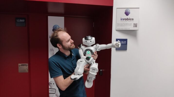 En la imagen aparece José Carlos, director técnico de Irobics, sujetando en brazos a el robot Nao. Se encuentra en la puerta de su oficina.