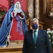 Juan Venegas, Hermano Mayor de la Hermandad de los Estudiantes de Madrid, vestido con traje y corbata. Dentro de la Basílica Pontificia de San Miguel junto a la imagen de la Virgen.