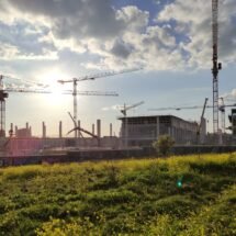Edificio en construcción de la nueva Fábrica de Moneda y Timbre situada en Vicálvaro, rodeada de grúas y de un extenso prado verde.