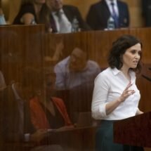 Presidenta de la Comunidad de Madrid Isabel Díaz Ayuso, con camisa blanca, hablando en alto, ayudándose de un micrófono.