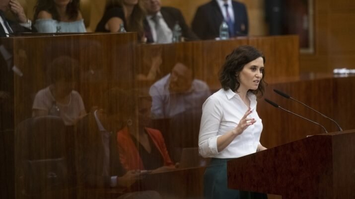 Presidenta de la Comunidad de Madrid Isabel Díaz Ayuso, con camisa blanca, hablando en alto, ayudándose de un micrófono.