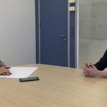 Periodista y entrevistada hablando en una sala de reuniones con distancia de seguridad y mascarillas