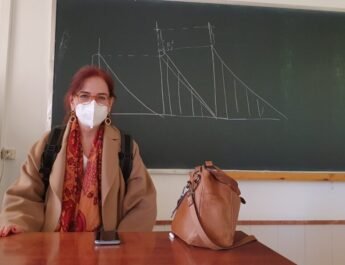 María Nieves San Emeterio posa sentada en la mesa del profesor, con mascarilla. Detrás de ella se encuentra la pizarra en la que ha dibujado gráficas.