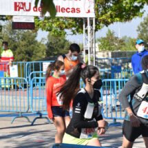 Nueve corredores vestidos con la equipación y mascarilla. Al fondo se ve un cartel de PAU de Vallecas. De día.