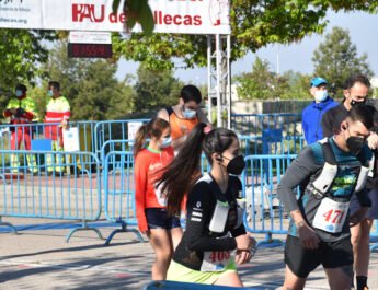 Nueve corredores vestidos con la equipación y mascarilla. Al fondo se ve un cartel de PAU de Vallecas. De día.