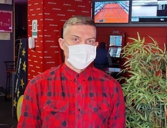 Alejandro Sánchez, propietario de seis casas de apuestas, vestido de rojo y con mascarilla mirando frente a la cámara dentro su salón de juegos en Pinto