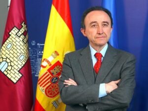 Fernando Lamata, hombre mayor de pie con fondo azul y la Banderas de España y Catilla La Mancha