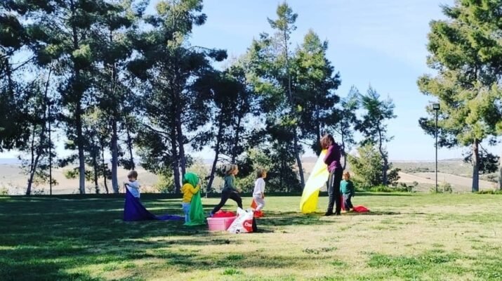 Cinco niños realizando aprendizaje experimental en un prado rodeado de árboles junto a su mamá de día