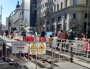 Calle Gran Vía a la altura de la calle Montera. Se ven las vallas de las obras y personas caminando entre ellas. De día.