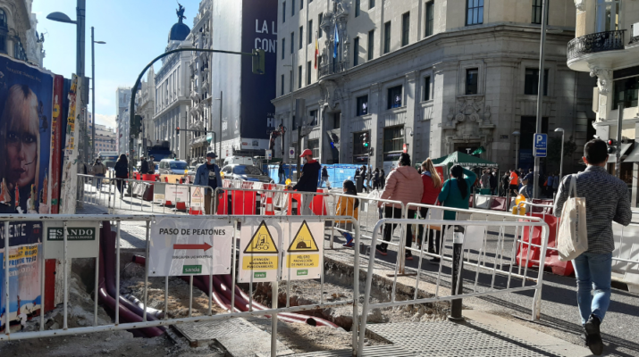 Calle Gran Vía a la altura de la calle Montera. Se ven las vallas de las obras y personas caminando entre ellas. De día.