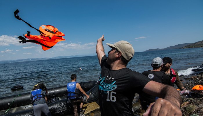 Un refugiado lanzando el chaleco salvavidas tras llegar a tierra después de su travesía de Turquía a Grecia