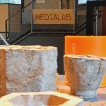 Una serie de recipientes elaborados con materiales reciclados y de fondo un cartel de Medialab