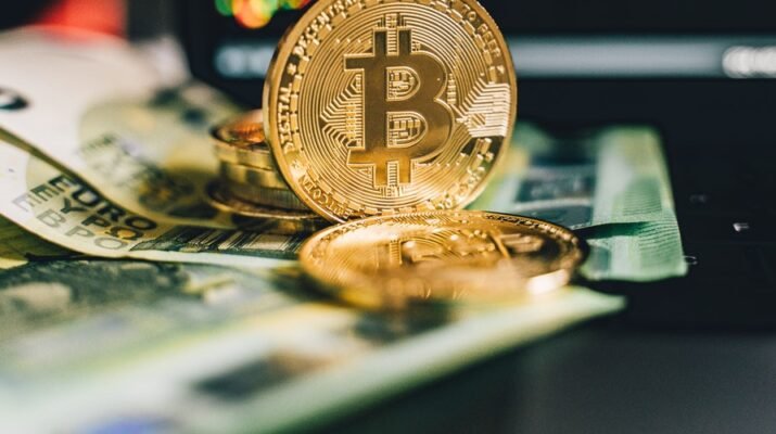 Monedas bitcoin en forma de euro, apoyadas sobre unos billetes de 100 euros.