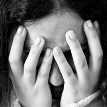 Rostro de una mujer en primer plano que, con las manos, se tapa la cara totalmente. Imagen en blanco y negro.