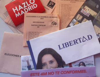 Varios sobres y papeletas de las elecciones de Madrid en 2021. Aparecen esparcidos por una mesa con luz de día.