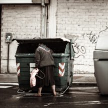 Una mujer buscando en un contenedor de basura.