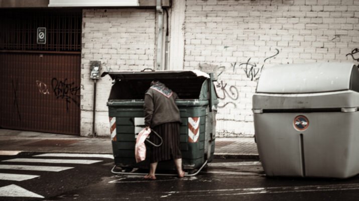 Una mujer buscando en un contenedor de basura.