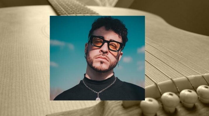 El cantante Jonathan Pons, joven moreno con barba y cabello rizado vestido de negro con una cadena al cuello y gafas mira a cámara sobre un cielo azul. Está superpuesto sobre una fotografía en sepia de una guitarra