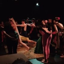 Actores sobre escenario bailando formando un corro.