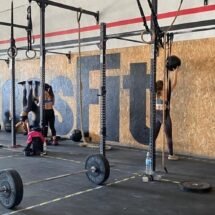 Un gimnasio de CrossFit en el que se realizan diferentes ejercicios para fortalecer la musculatura. Aparecen varios deportistas entrenando, levantando pesas y estirándose. También se ven aparatos del gimnasio, como máquinas para levantar pesas o barras para hacer flexiones.