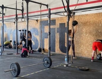 Un gimnasio de CrossFit en el que se realizan diferentes ejercicios para fortalecer la musculatura. Aparecen varios deportistas entrenando, levantando pesas y estirándose. También se ven aparatos del gimnasio, como máquinas para levantar pesas o barras para hacer flexiones.