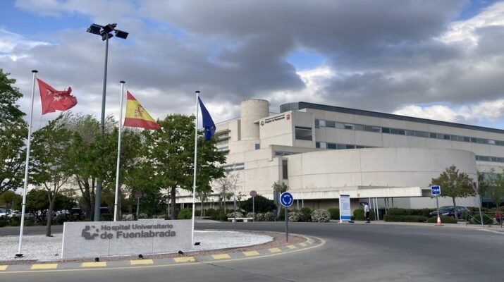 Hospital visto desde el exterior. A la izquierda una rotonda con banderas y a la derecha el edificio.