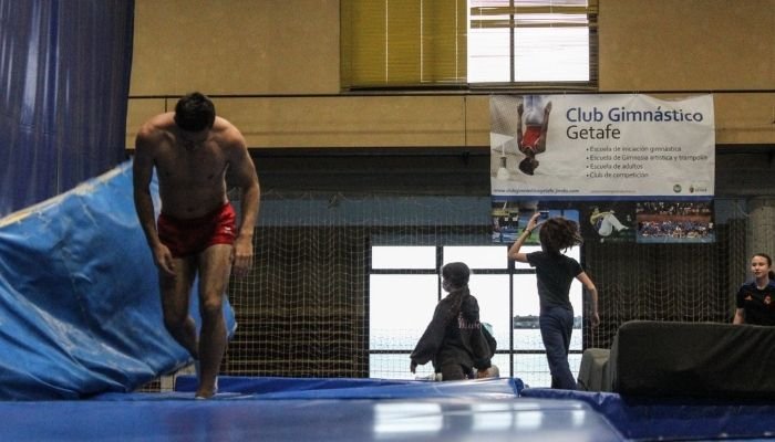 Hombre sin camiseta con pantalones cortos rojos mientras entrena. Está en un espacio interior. Tiene la cabeza baja.