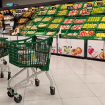 Dos carros de la compra de color verde situados frente a la frutería de un supermercado español. No hay personas en la escena.
