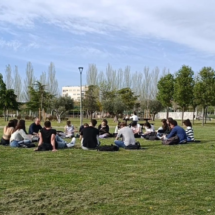 Estudiantes de la URJC sentados en círculo en el césped del campus de Fuenlabrada bajo el sol