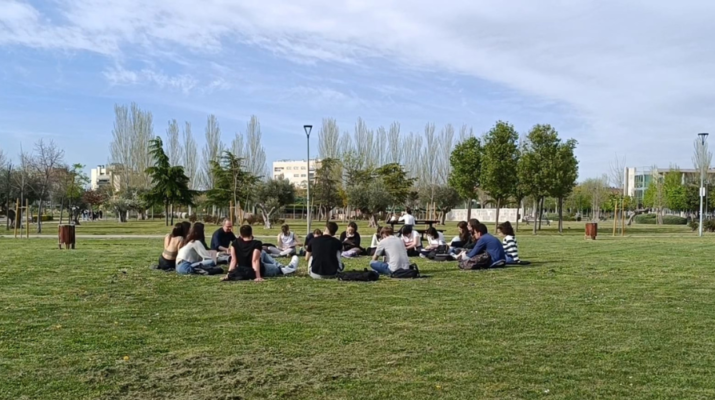 Estudiantes de la URJC sentados en círculo en el césped del campus de Fuenlabrada bajo el sol