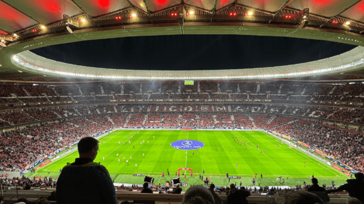 Imagen del terreno de juego y panorámica de la grada del Estadio Metropolitano, donde se puede ver a personas asistentes a un partido y una tela en el centro del campo.