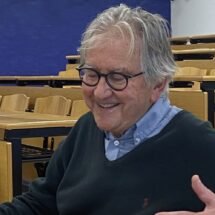 En la imagen podemos observar a Joaquín Rábago sonriente en un aula de la Universidad Rey Juan Carlos con un fondo azul.