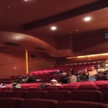 Sala del Teatro Josep Carreras justo antes de comenzar una obra de teatro donde se ven personas que han acudido al evento esperando sentadas tranquilamente.