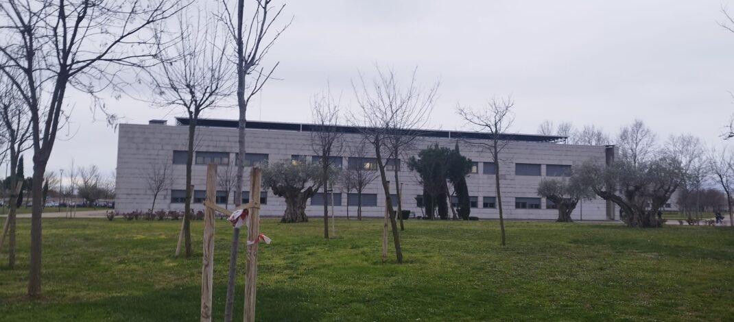 La imagen muestra un plano opanorámico del campus de Feunlabrada. Hay césped colorido y alho húmedo, un edificio grisáceo y rectángular frente el objetivo y varios árboles esbeltos a lo largo del plano. Asimismo el cielo está completamente encapotado.