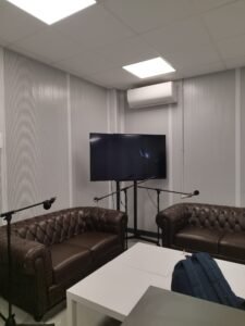 Imagen del plató donde se graba el videopodcast con dos sofás de cuero, micrófonos y una televisión