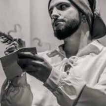 Luca Arbore sujeta un libro vestido de pirata con un paño en la cabeza y una camisa blanca holgada. La fotografía está en blanco y negro.