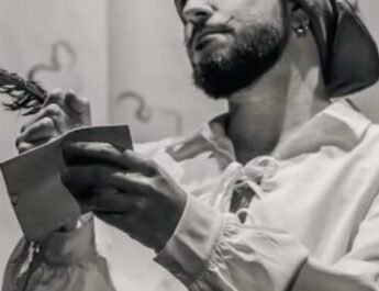 Luca Arbore sujeta un libro vestido de pirata con un paño en la cabeza y una camisa blanca holgada. La fotografía está en blanco y negro.