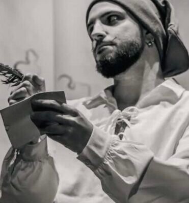 Luca Arbore sujeta un libro vestido de pirata con un paño en la cabeza y una camisa blanca holgada. La fotografía está en blanco y negro.