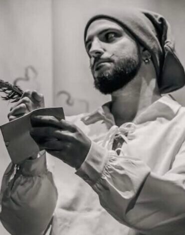 Luca Arbore sujeta un libro vestido de pirata con un paño en la cabeza y una camisa blanca holgada. La fotografía está en blanco y negro.