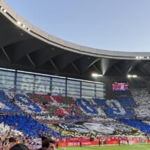 imagen de un estadio de fútbol de sevillanas con un mosaica en un lateral con la ikurriña, una imagen de Aitor Zabaleta en blanco y negro y dos lineas grandes azules y blancas