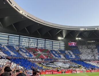 imagen de un estadio de fútbol de sevillanas con un mosaica en un lateral con la ikurriña, una imagen de Aitor Zabaleta en blanco y negro y dos lineas grandes azules y blancas