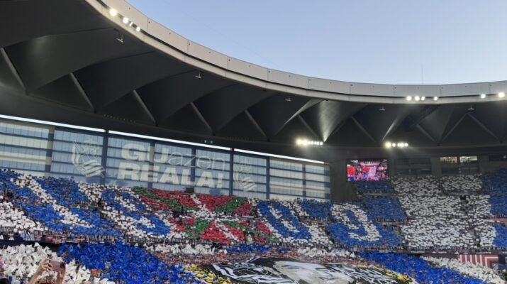 imagen de un estadio de fútbol de sevillanas con un mosaica en un lateral con la ikurriña, una imagen de Aitor Zabaleta en blanco y negro y dos lineas grandes azules y blancas