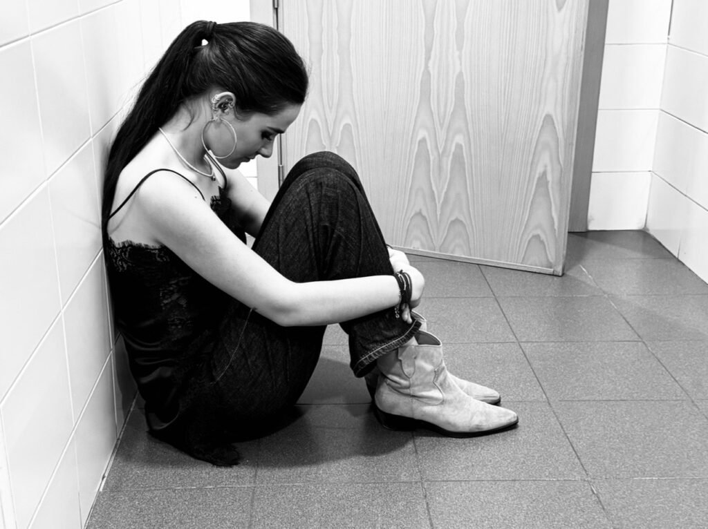 Chica sentada a la salida de un baño triste