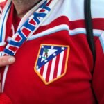 Un aficionado del Atlético de Madrid señala el escudo de su camiseta con el dedo.