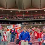 Aficionados del Atlético de Madrid levantan sus brazos, banderas y bufandas para animar a su equipo en la grada