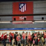 Aficionados del Atlético de Madrid, con camisetas del equipo, esperan al metro en la parada de Estadio Metropolitano. La pared superior del andén está decorada con un escudo del equipo y el número 1947, la fecha de su creación.