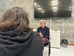 Javier de la Cueva sentado siendo entrevistado por Karen Cano en una habitación cerrada. El entrevistado está de frente y al entrevistador se le ve de espaldas a la cámara