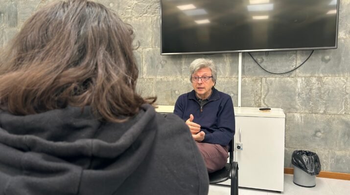 Javier de la Cueva sentado siendo entrevistado por Karen Cano en una habitación cerrada. El entrevistado está de frente y al entrevistador se le ve de espaldas a la cámara